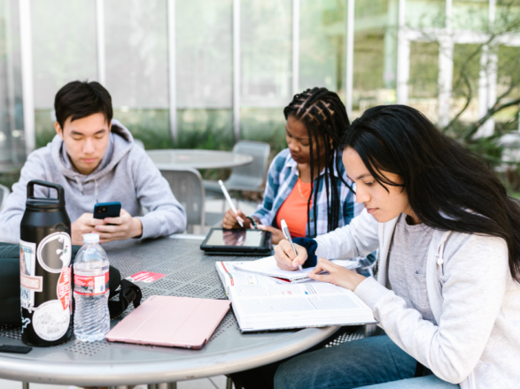 Trois jeunes étudiants assis autour d'une table qui font leurs devoirs